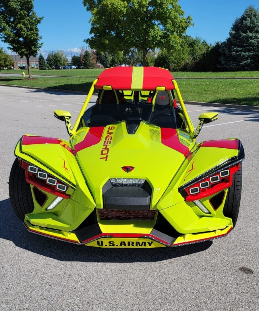 Bright yellow and red Slingshot vehicle with U.S. Army branding parked outside on a sunny day.