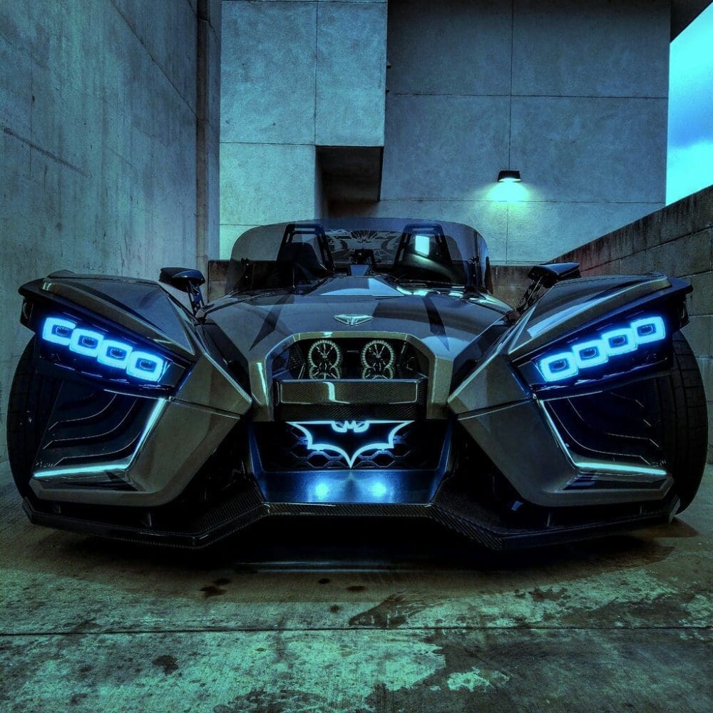 Futuristic black car with glowing blue headlights and a Batman logo.