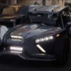 A sleek black three-wheeled vehicle with modern LED headlights on a street.