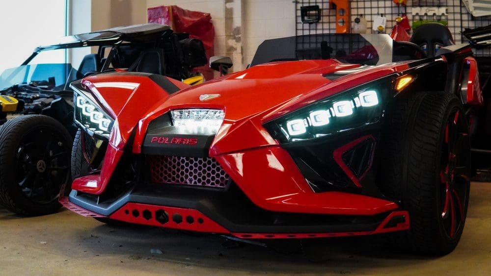 Red Polaris three-wheeled vehicle with futuristic headlights in a garage.