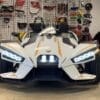 Front view of a sleek white Polaris three-wheeled vehicle with illuminated headlights.
