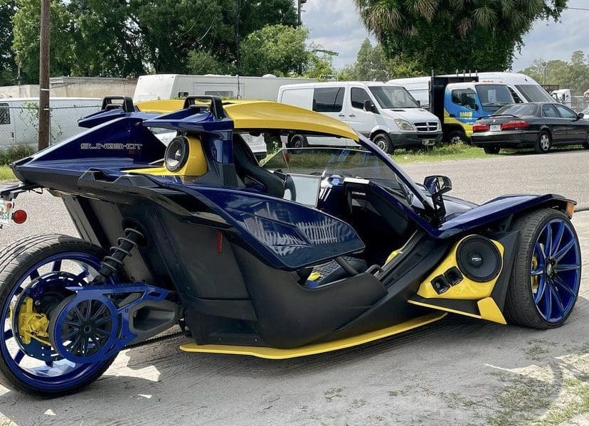 IMG-3207 Sleek three-wheeled vehicle with blue and yellow design.