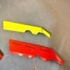 fender spliters Two plastic car bumper covers, one yellow and one red, lying on the ground.