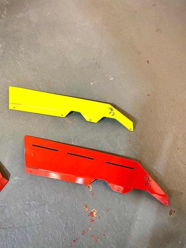fender spliters Two plastic car bumper covers, one yellow and one red, lying on the ground.