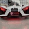 A futuristic white three-wheeled vehicle with red lights in a garage.