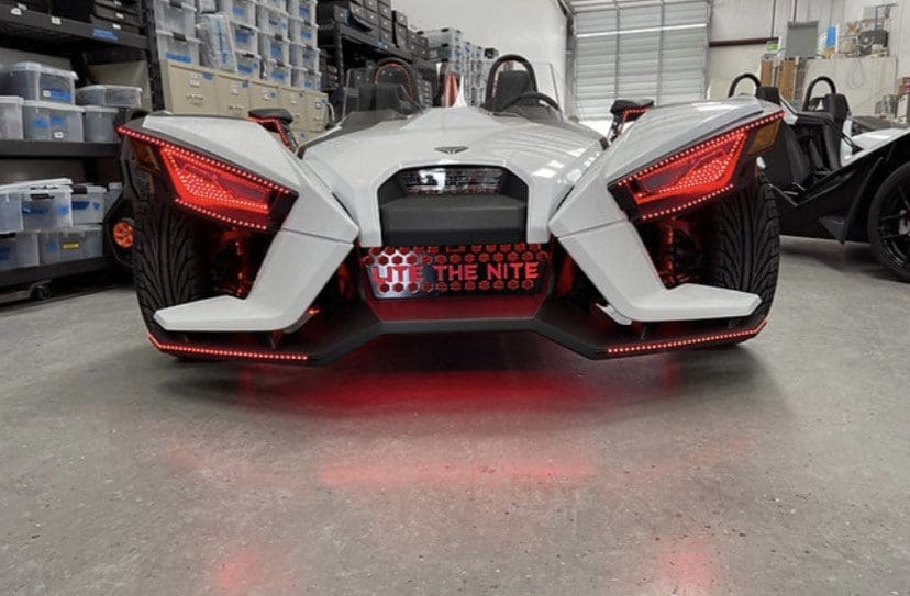 A futuristic white three-wheeled vehicle with red lights in a garage.