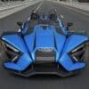 A sleek, blue three-wheeled sports car on a city street.
