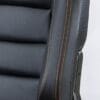 Close-up of a black leather chair with orange stitching and carbon fiber accents.