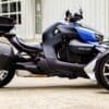 A sleek Can-Am three-wheeled motorcycle parked on concrete outside a building.
