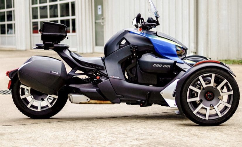 A sleek Can-Am three-wheeled motorcycle parked on concrete outside a building.