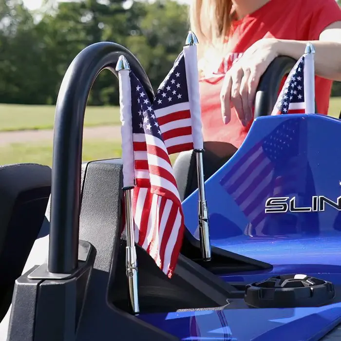 44-104_folding-flag-pole-on-slingshot_lifestyle_1 Two small American flags attached to a blue vehicle with a person in the background.