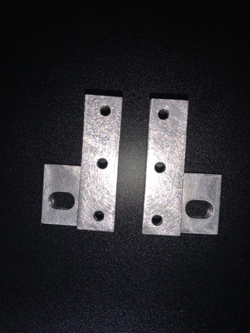 IMG_6728 Two metal brackets with multiple holes on a black background.