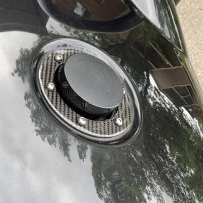 Close-up of a black car's fuel cap on a shiny surface.