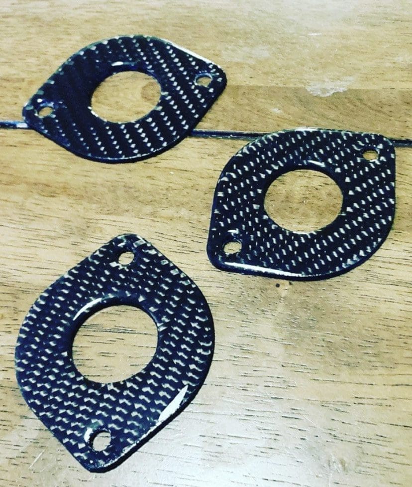 IMG_6986 Three black carbon fiber washers with different shapes on a wooden surface.