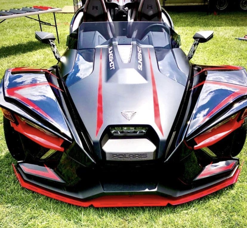 IMG_7279 A sleek black and red Polaris Slingshot parked on grass.