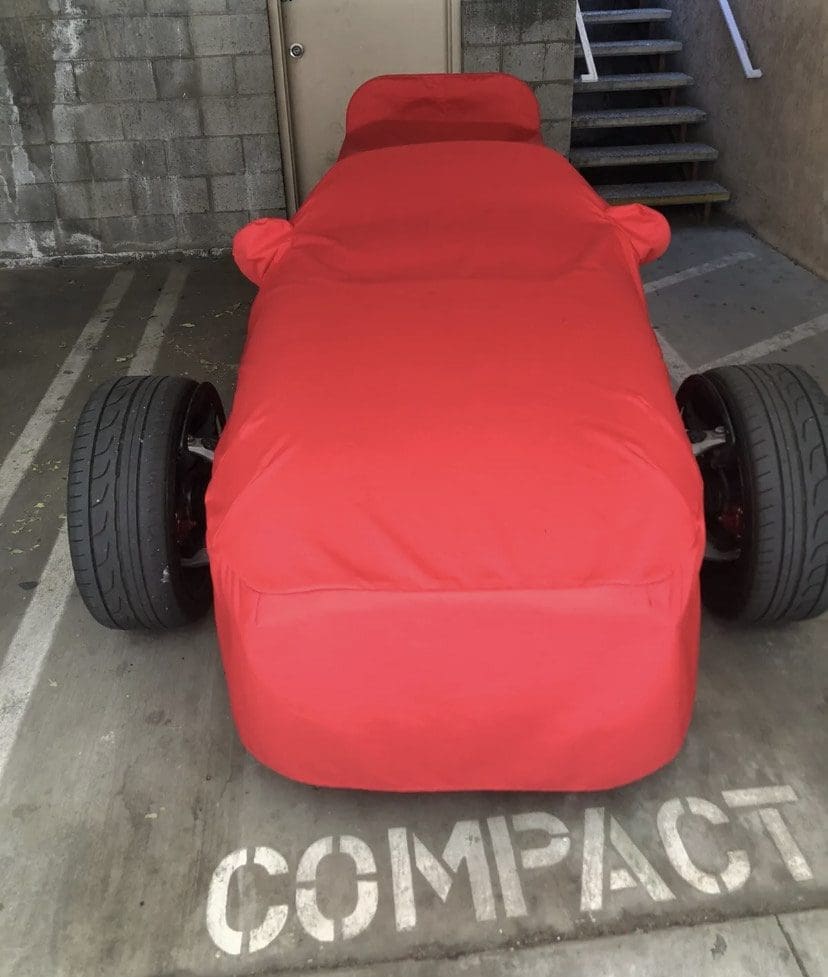 IMG_8046 A small race car covered in a red cloth in a parking space.