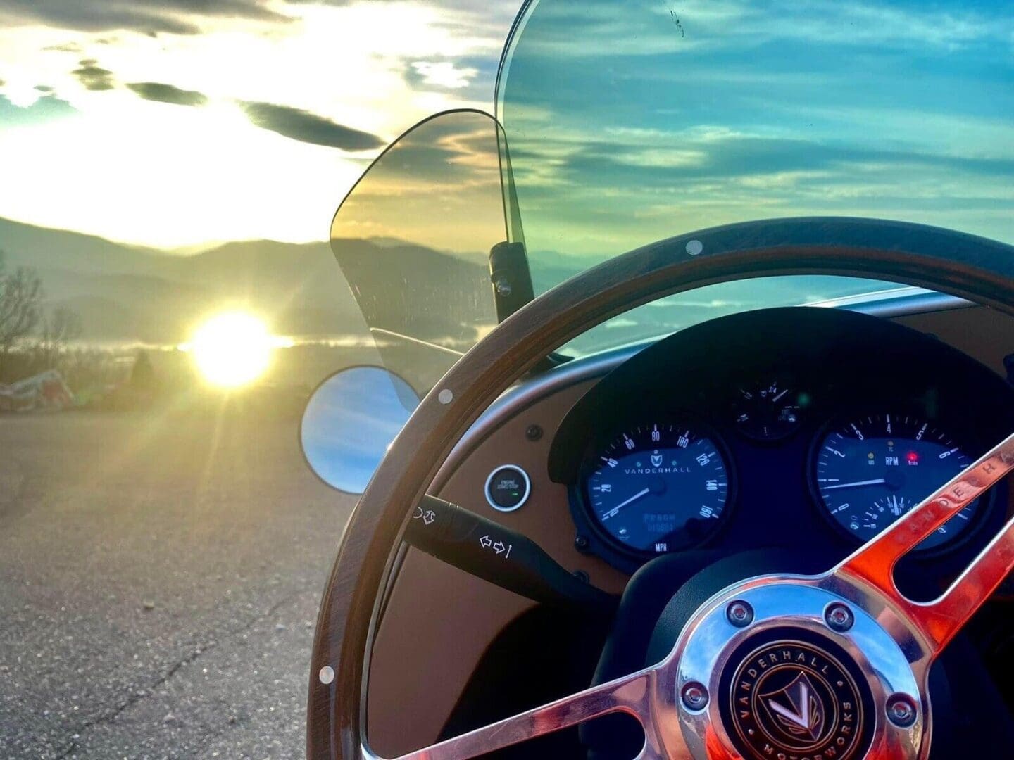 View from a car's steering wheel with sunset and sun flare in the background.