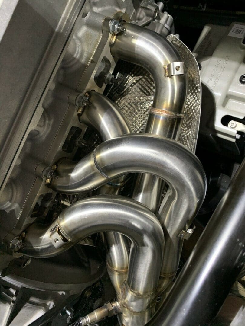 Close-up of polished stainless steel exhaust headers in an engine bay.