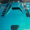 2594fc_d0f7baec527d4fe2b9c95866d04fd106~mv2 Close-up of a teal car hood with a hood scoop and black lettering decals.