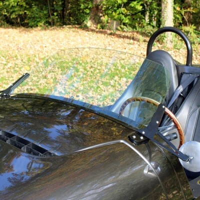 Close-up of a vintage car's cockpit with a curved windshield and leather seat.