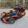 img_0861 Orange and black three-wheeled sports vehicle parked outdoors.
