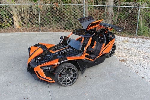 img_0861 Orange and black three-wheeled sports vehicle parked outdoors.