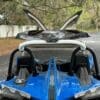 img_0862-2 Two blue sports cars parked side by side with open hoods.